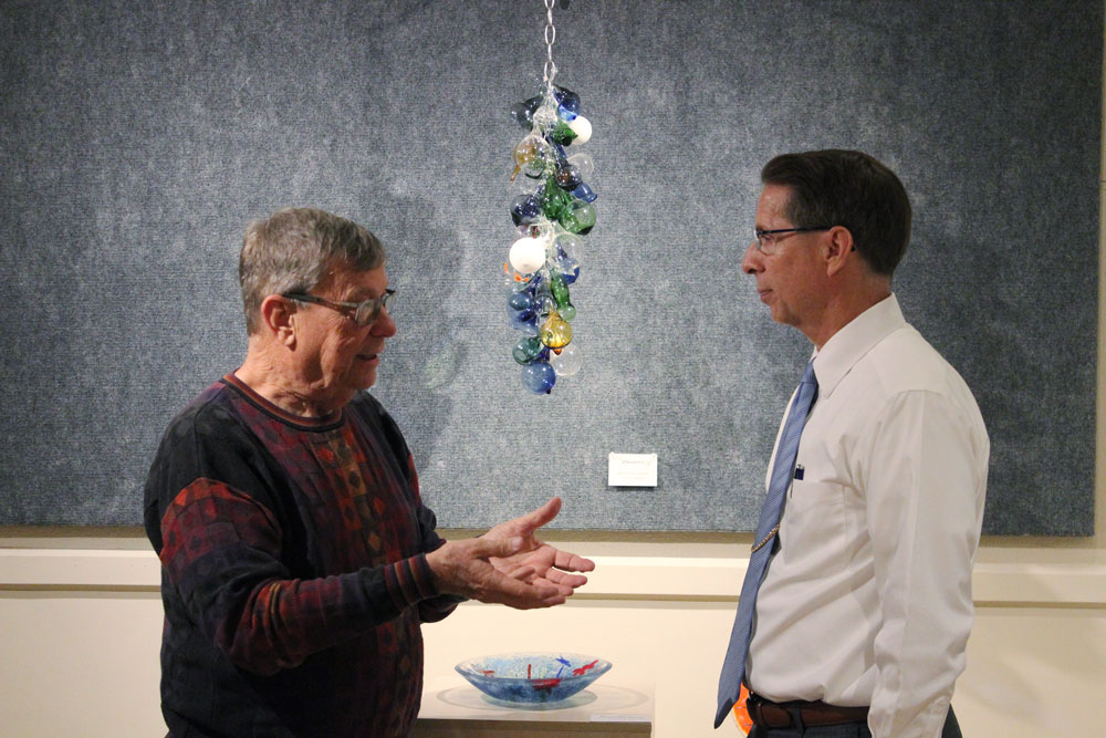 Keith Wilson, left, of ChaGlaz Designs in Glass of Parsons, talks with Labette Community College President Dr. Mark Watkins during the Meet & Greet on Tuesday. ChaGlaz Designs in Glass is the current art exhibit in the LCC Hendershot Gallery which hosted a meet and greet for the community to visit with Charlean and Keith Wilson. The Parsons based glass art studio of the Wilsons, began more than 10 years ago as a hobby. Today, the couple sell their glass designs on the web and at art shows.